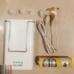 TIANLE HA-2000 hearing aid device with earpieces cables and Panasonic AA battery on flat surface